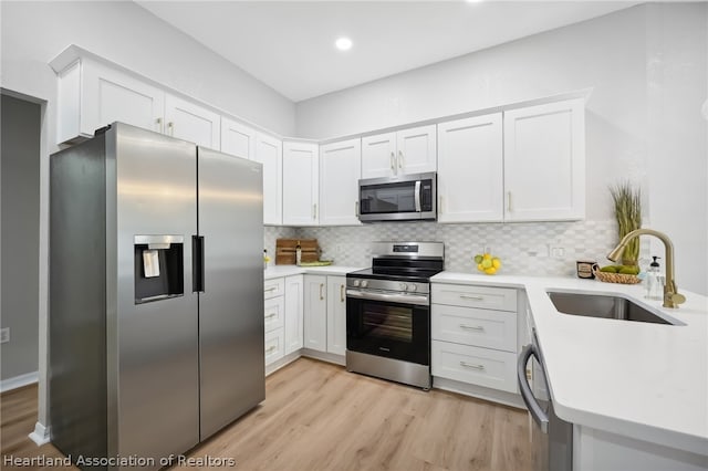 kitchen featuring white cabinetry, sink, stainless steel appliances, light hardwood / wood-style flooring, and backsplash