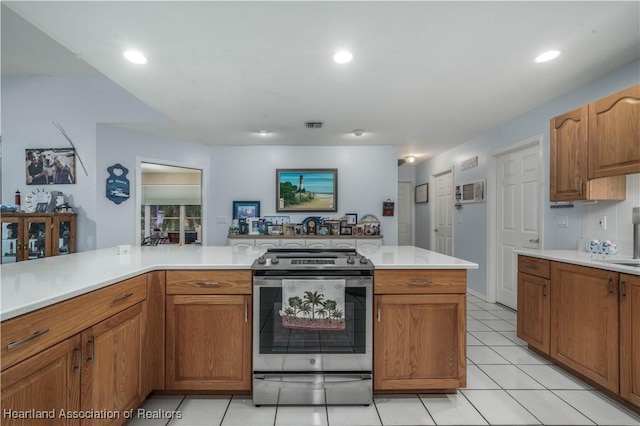 kitchen featuring light tile patterned floors, stainless steel gas range oven, visible vents, brown cabinets, and light countertops