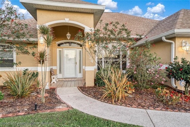 entrance to property featuring a shingled roof and stucco siding