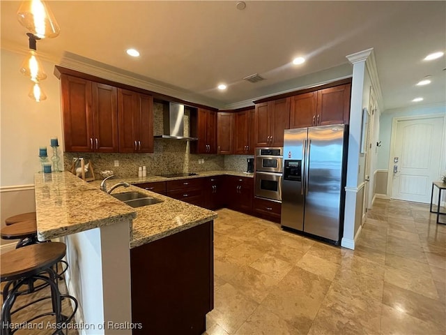 kitchen with sink, wall chimney exhaust hood, hanging light fixtures, stainless steel appliances, and a breakfast bar area