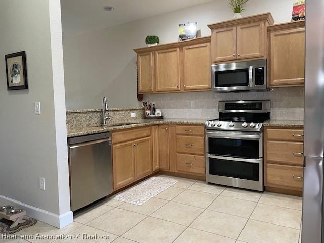 kitchen featuring stainless steel appliances, light stone counters, tasteful backsplash, and sink