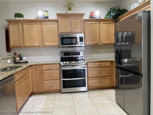 kitchen featuring tasteful backsplash, sink, light tile patterned flooring, appliances with stainless steel finishes, and light stone counters