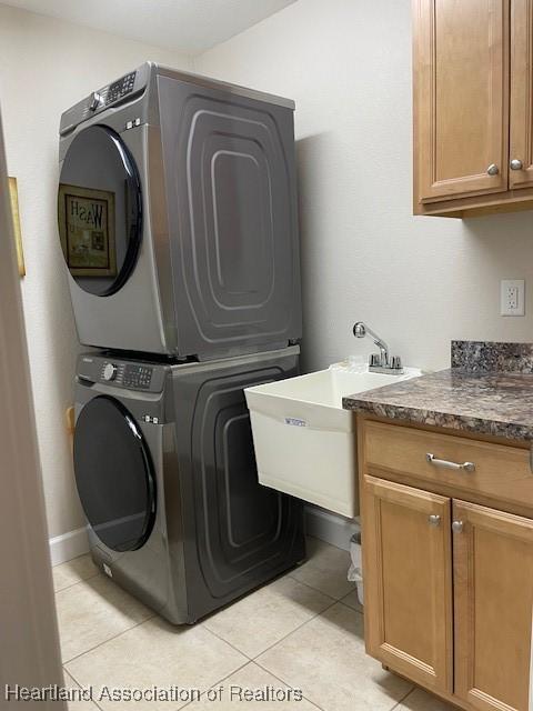 clothes washing area with cabinets, stacked washer and clothes dryer, sink, and light tile patterned flooring