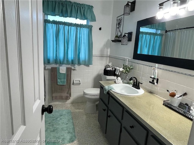 full bath featuring vanity, speckled floor, wainscoting, tile walls, and toilet