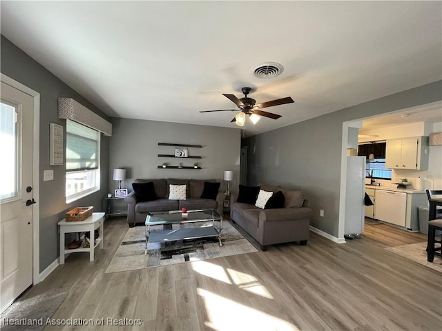 living area with a ceiling fan, visible vents, baseboards, and light wood-type flooring