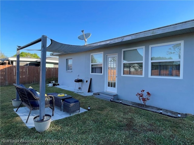 rear view of property featuring stucco siding, a lawn, a patio area, and fence