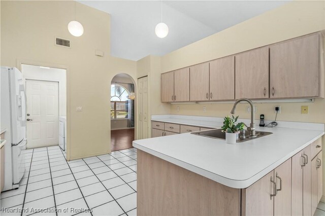 kitchen featuring kitchen peninsula, sink, white refrigerator with ice dispenser, light brown cabinets, and hanging light fixtures