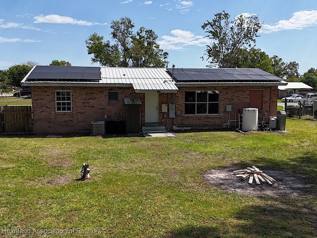 rear view of property with central AC unit, a lawn, fence, and roof mounted solar panels