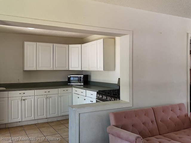 kitchen featuring light tile patterned flooring, black microwave, stainless steel gas stove, and white cabinetry