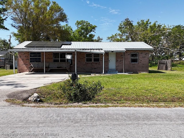 ranch-style home featuring metal roof, a front lawn, brick siding, and roof mounted solar panels