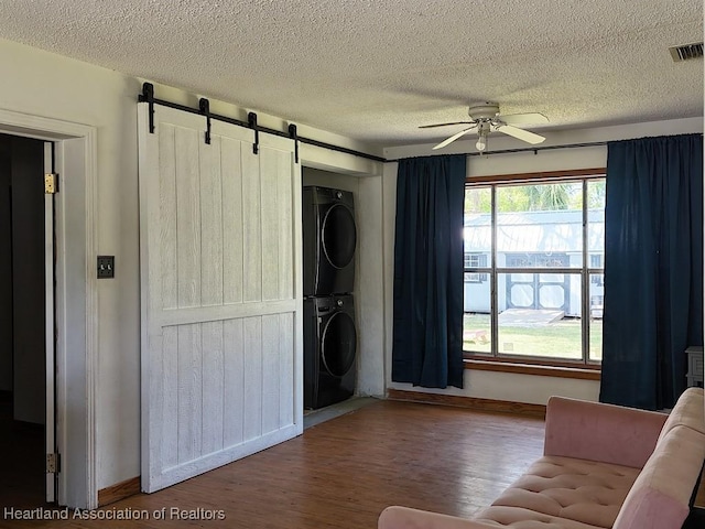 unfurnished living room featuring stacked washer and dryer, visible vents, a barn door, a ceiling fan, and wood finished floors