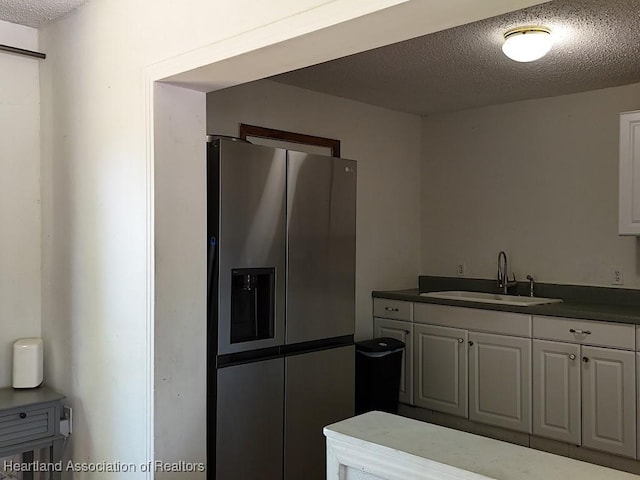 kitchen with a textured ceiling, dark countertops, a sink, and stainless steel fridge with ice dispenser