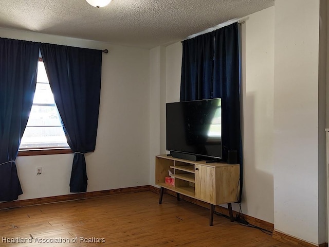 unfurnished living room featuring a textured ceiling, baseboards, and wood finished floors