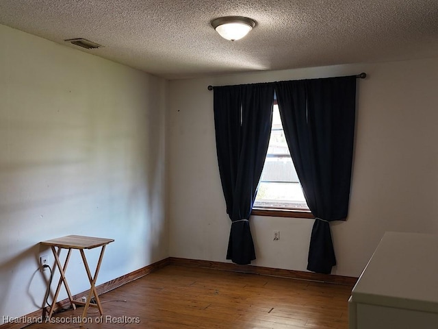 empty room featuring a textured ceiling, wood finished floors, visible vents, and baseboards