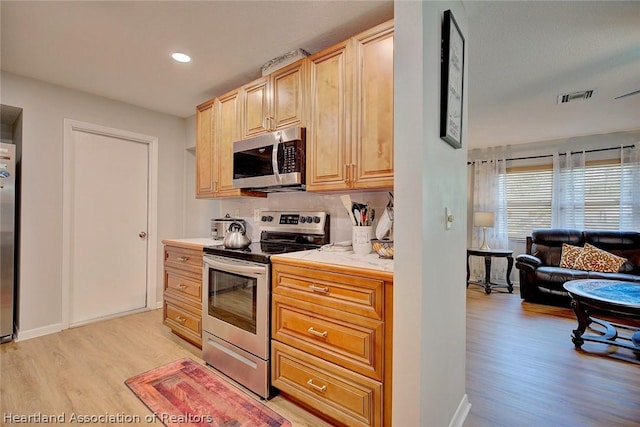 kitchen featuring decorative backsplash, light brown cabinetry, stainless steel appliances, and light wood-type flooring