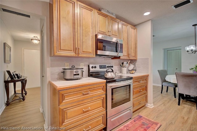 kitchen featuring hanging light fixtures, a chandelier, decorative backsplash, appliances with stainless steel finishes, and light wood-type flooring