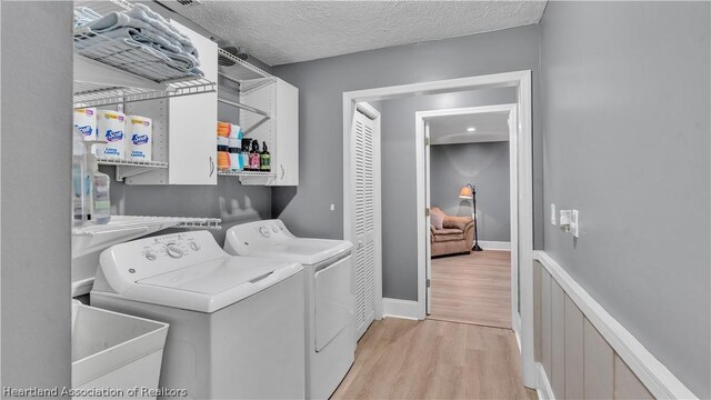 washroom with cabinets, sink, independent washer and dryer, a textured ceiling, and light hardwood / wood-style floors