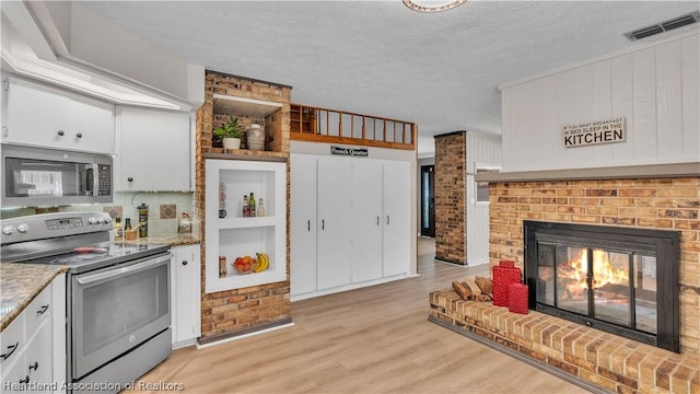 kitchen with stainless steel appliances, light hardwood / wood-style flooring, a textured ceiling, a fireplace, and white cabinets