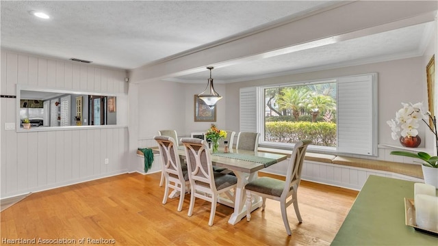 dining area with hardwood / wood-style floors, ornamental molding, a textured ceiling, and wooden walls