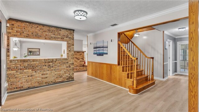 interior space with brick wall, ornamental molding, wood walls, a textured ceiling, and light wood-type flooring