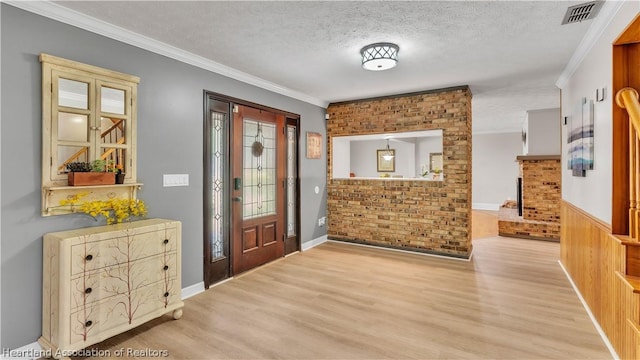 entryway with wooden walls, light wood-type flooring, a textured ceiling, and ornamental molding