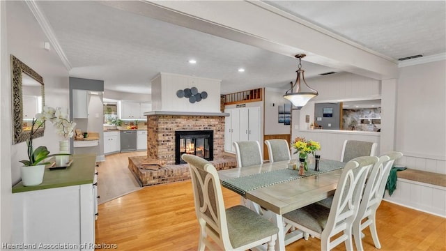 dining area featuring light wood-type flooring, ornamental molding, and a brick fireplace