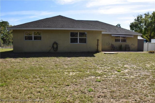 back of property featuring stucco siding, roof with shingles, a patio, and a yard