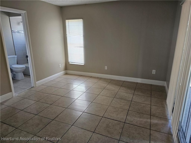 unfurnished bedroom with light tile patterned floors and connected bathroom