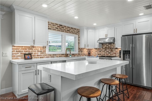 kitchen with a kitchen breakfast bar, white cabinets, dark hardwood / wood-style floors, a kitchen island, and appliances with stainless steel finishes