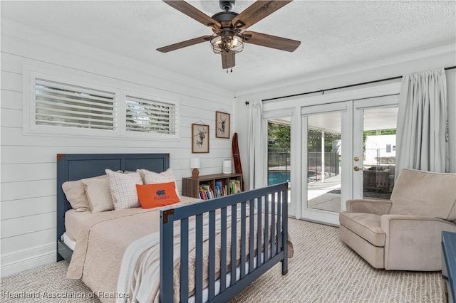 bedroom featuring access to exterior, a textured ceiling, ceiling fan, and wood walls