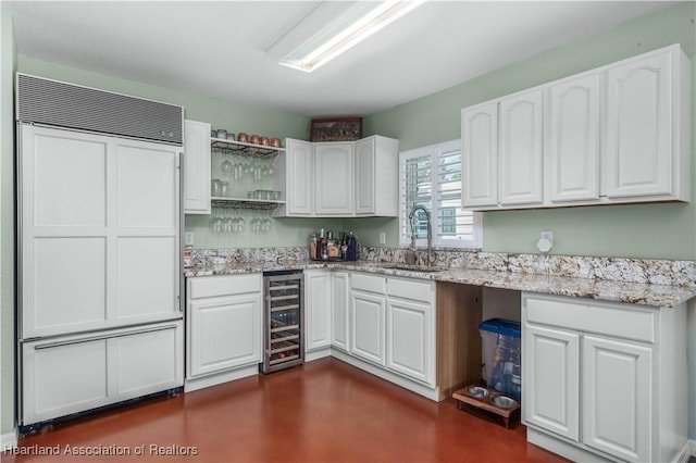 kitchen with sink, wine cooler, light stone counters, paneled built in fridge, and white cabinets