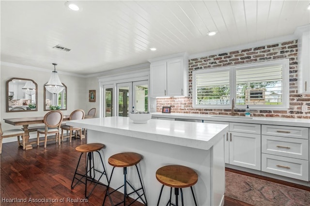 kitchen featuring dark wood-type flooring, a kitchen island, brick wall, pendant lighting, and white cabinets