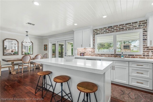 kitchen featuring dark wood-type flooring, a kitchen island, brick wall, pendant lighting, and white cabinets