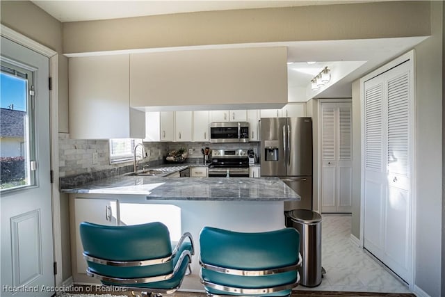 kitchen featuring sink, tasteful backsplash, white cabinetry, kitchen peninsula, and stainless steel appliances