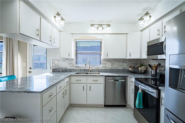 kitchen featuring white cabinetry, sink, kitchen peninsula, dark stone countertops, and appliances with stainless steel finishes