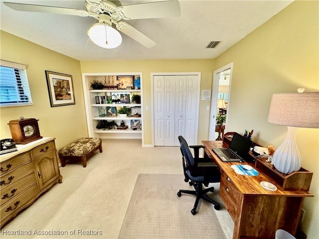 carpeted home office with ceiling fan and built in shelves