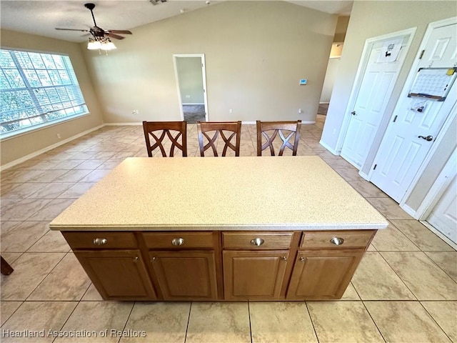 kitchen featuring light tile patterned floors, a ceiling fan, light countertops, vaulted ceiling, and a center island