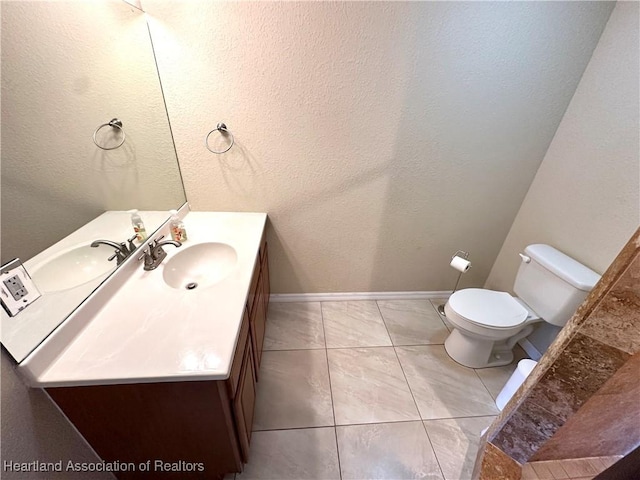 bathroom featuring vanity, baseboards, tile patterned flooring, toilet, and a textured wall