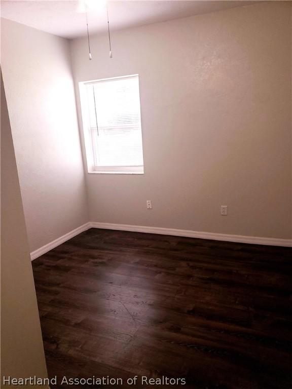 unfurnished room featuring dark wood-style floors and baseboards