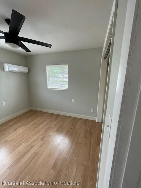 unfurnished bedroom featuring a wall mounted AC, ceiling fan, and light hardwood / wood-style flooring