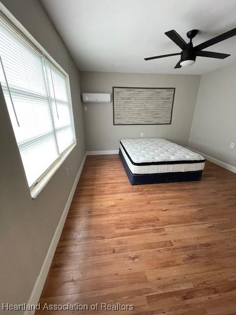 unfurnished bedroom featuring a wall unit AC, ceiling fan, and hardwood / wood-style flooring