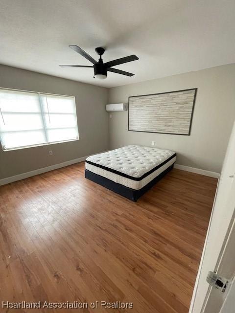 unfurnished bedroom with wood-type flooring, an AC wall unit, and ceiling fan