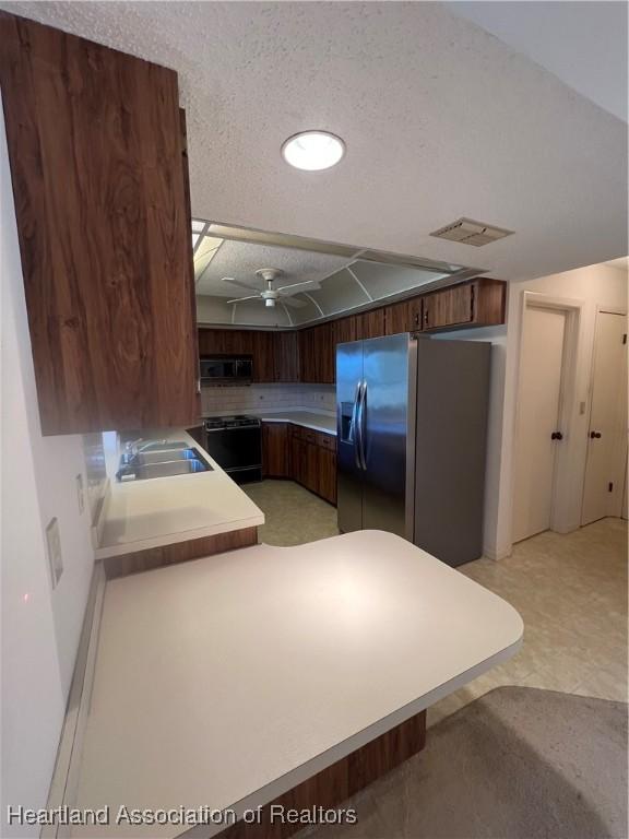 kitchen with kitchen peninsula, stainless steel refrigerator with ice dispenser, black range with electric cooktop, a textured ceiling, and sink