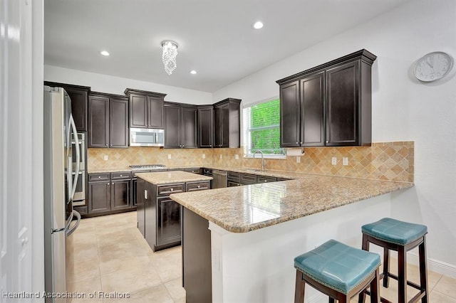 kitchen featuring light stone countertops, a center island, kitchen peninsula, a kitchen bar, and appliances with stainless steel finishes