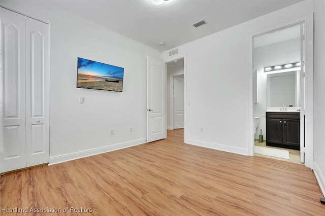 unfurnished bedroom featuring connected bathroom, light hardwood / wood-style flooring, and a closet