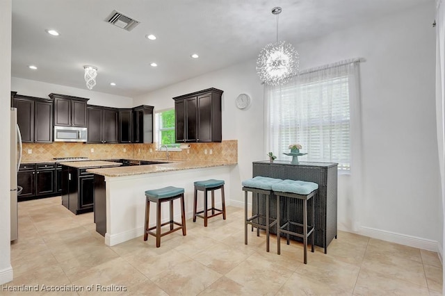 kitchen featuring kitchen peninsula, appliances with stainless steel finishes, backsplash, pendant lighting, and an inviting chandelier