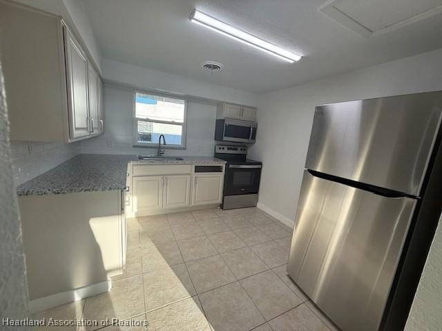 kitchen with white cabinetry, sink, stainless steel appliances, light stone counters, and light tile patterned floors