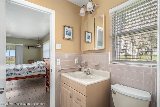 bathroom featuring wainscoting, toilet, ensuite bathroom, vanity, and tile walls