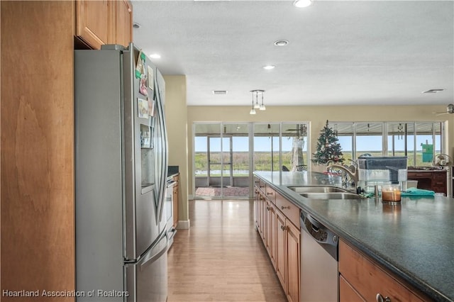 kitchen featuring light wood finished floors, dark countertops, brown cabinets, stainless steel appliances, and a sink