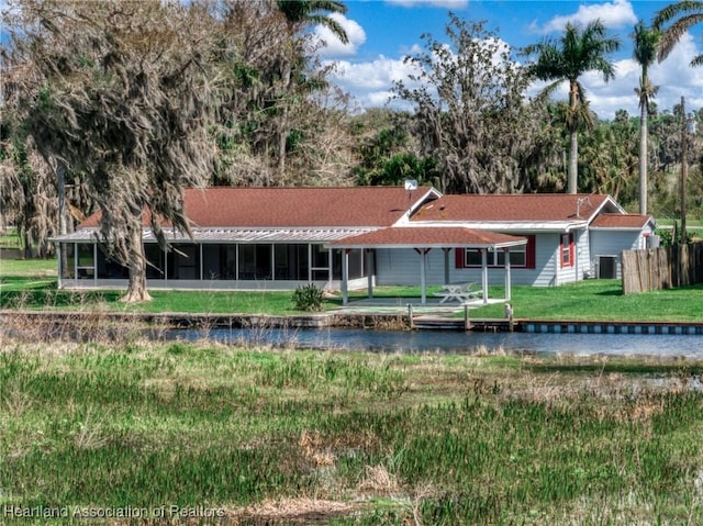 back of property with a water view, a sunroom, and a yard